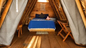 Ein gemütlicher, holzgetäfelter Raum im Zeltstil mit einem Bett, Kissen und einem hängenden Wandbehang aus Makramee.