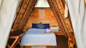Ein gemütlicher, dreieckiger Holzraum mit einem Bett, einem kleinen Tisch und einem Stuhl.