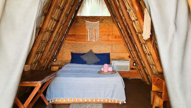A cozy, triangular wooden room with a bed, a small table, and a chair.
