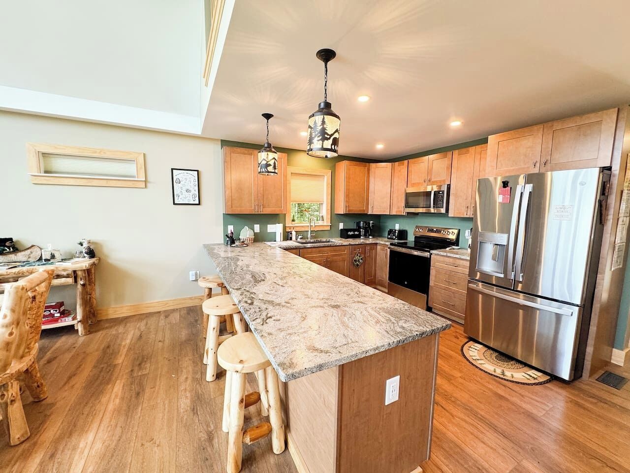 A modern kitchen with a central island, wooden bar stools, stainless steel appliances, and pendant lighting.