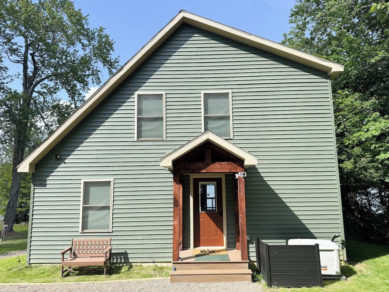 A two-story house with a front porch, a wooden bench, and a mailbox.