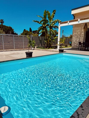 A clear blue pool with a white edge, surrounded by a patio area with chairs and a table, and a palm tree in the background. - Villa Zagara, a villa with a pool where families and friends can relax (Piane Vecchie)