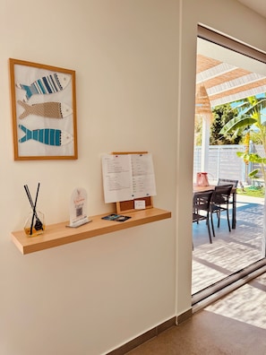 A reception area with a framed fish artwork, a welcome sign, a corkboard with papers, a glass bottle with a label, and a book on a wooden shelf. - Villa Zagara, a villa with a pool where families and friends can relax (Piane Vecchie)