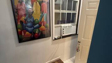 A hallway with a large abstract painting, a window with blinds, and a door.