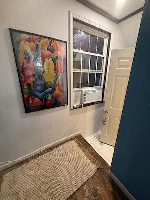 A hallway with a large abstract painting, a window with blinds, and a door.