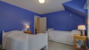 Een slaapkamer met twee enkele bedden, witte beddengoed en bedlampen.