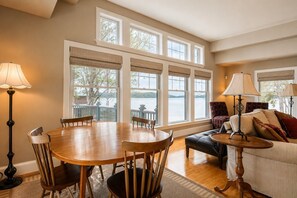 A dining area with a wooden table and chairs, a sofa with cushions, and a view of a lake through large windows. - Lakefront Estate | Private Beach | Dock | Luxury Retreat (Alton)