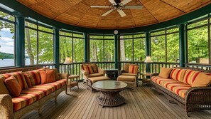 Un área de estar al aire libre, cubierta, con mobiliario de mimbre y una mesa central, con vista a un cuerpo de agua.