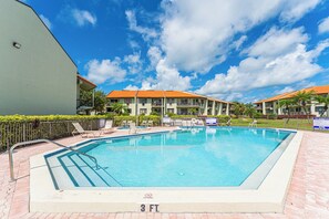 Ein rechteckiger Swimmingpool mit einer 3 Fuß tiefen Markierung, umgeben von Liegestühlen und einem Zaun, mit einem Gebäude im Hintergrund.