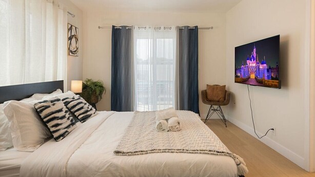 A modern bedroom with a bed, curtains, a television, and a plant. - Sun Chaser | Pool | Spacious Home | Parking (Monterey Park)