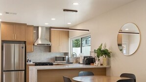 A modern kitchen with a central island, stainless steel appliances, and a dining area with chairs. - Sun Chaser | Pool | Spacious Home | Parking (Monterey Park)