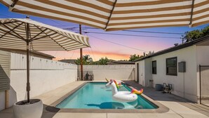 A backyard with a swimming pool, inflatable unicorn floaties, and striped umbrellas. - Sun Chaser | Pool | Spacious Home | Parking (Monterey Park)
