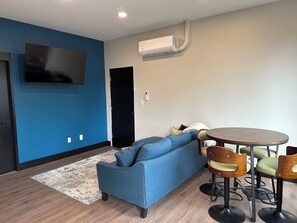 A modern living room with a blue sofa, a round dining table, and wooden chairs.