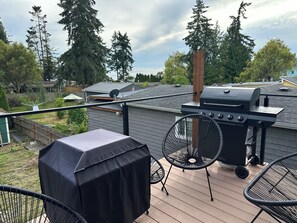 A rooftop patio with a grill, covered table, and chairs.