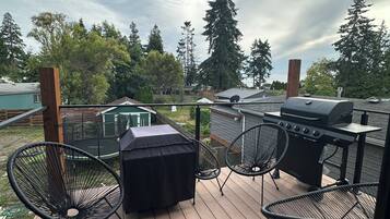 A deck with a grill, chairs, and a covered table.