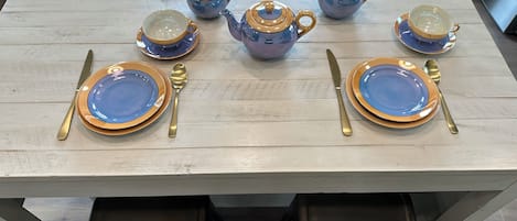 A dining table set with blue and gold plates, cutlery, and a teapot.