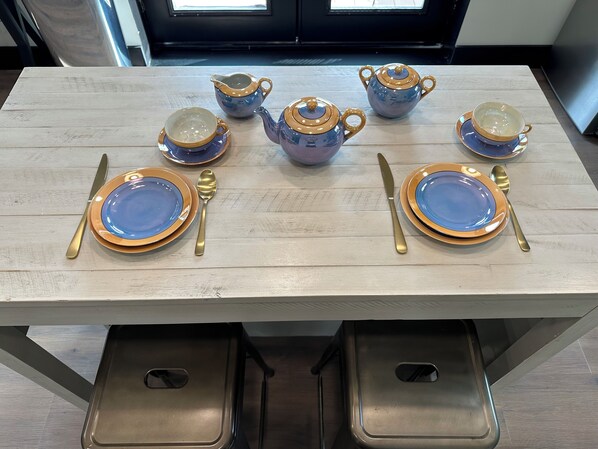 A dining table set with blue and gold plates, cutlery, and a teapot.