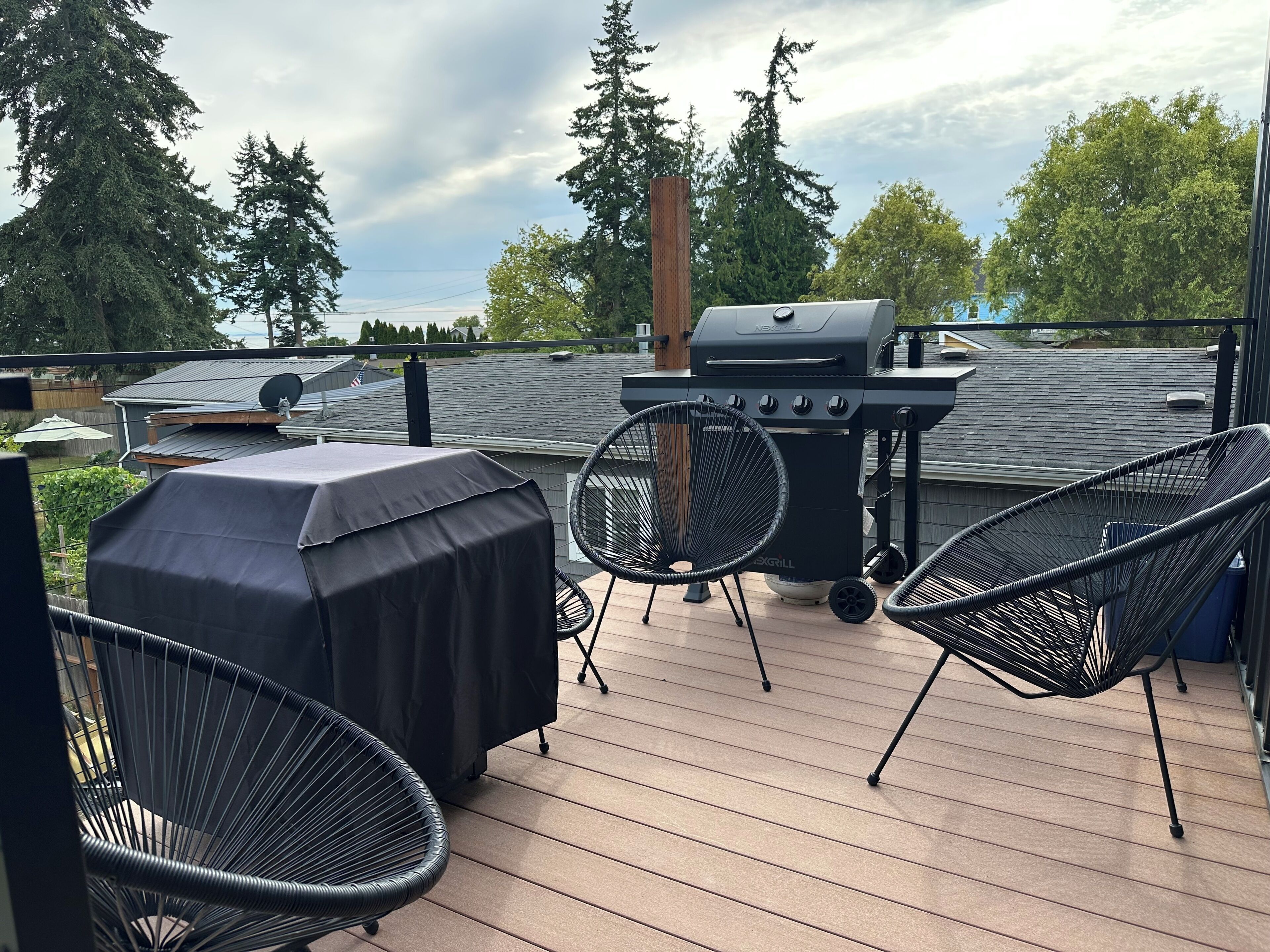 An outdoor deck with a barbecue grill, two chairs, and a covered table.