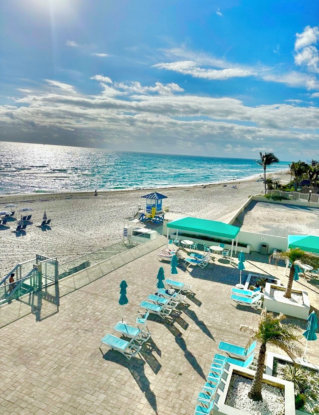 Un resort frente a la playa con piscina, tumbonas y un puesto de socorristas.