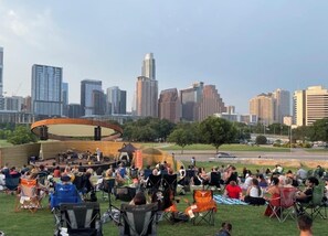 Eine Veranstaltung im Freien mit einer Bühne und Publikum in einem Park, im Hintergrund ist die Skyline einer Stadt zu sehen.