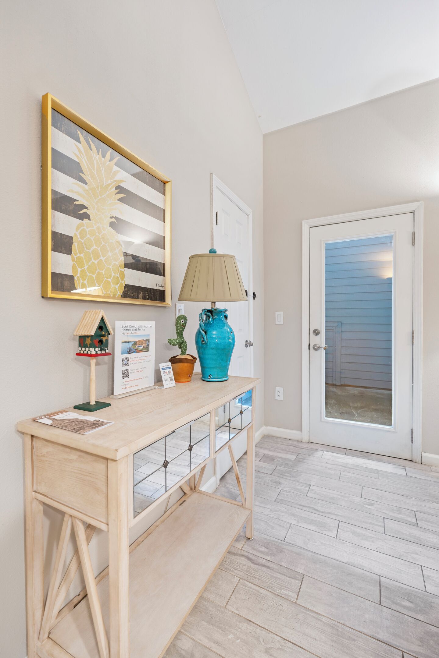 A wooden console table with a lamp, a pineapple artwork, and a cactus decoration.