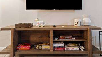 A flat-screen TV mounted on a wall above a wooden entertainment center with shelves containing books and board games.