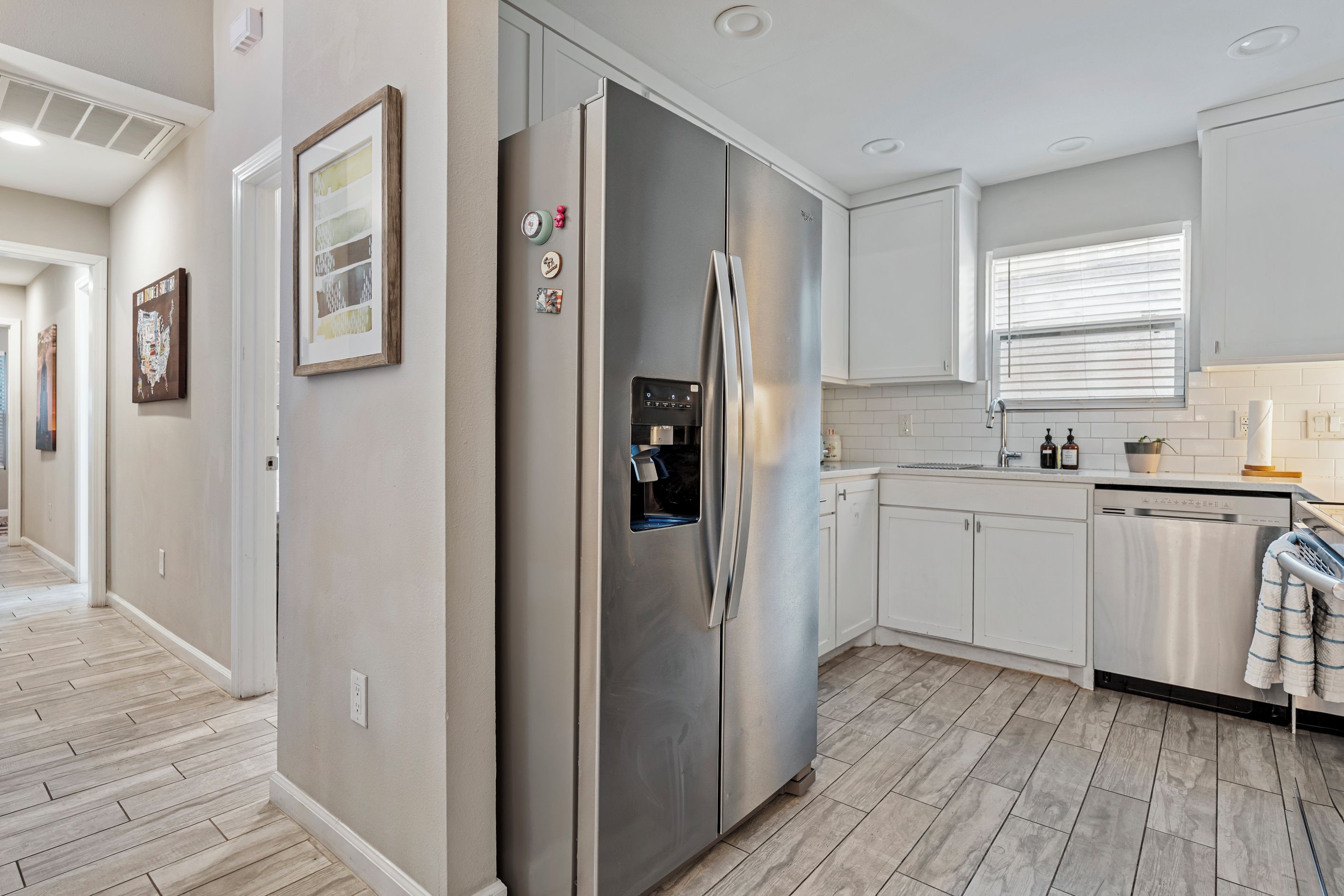 A modern kitchen with a stainless steel refrigerator, white cabinetry, and a wooden floor.