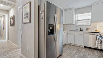 A modern kitchen with a stainless steel refrigerator, white cabinetry, and a wooden floor.