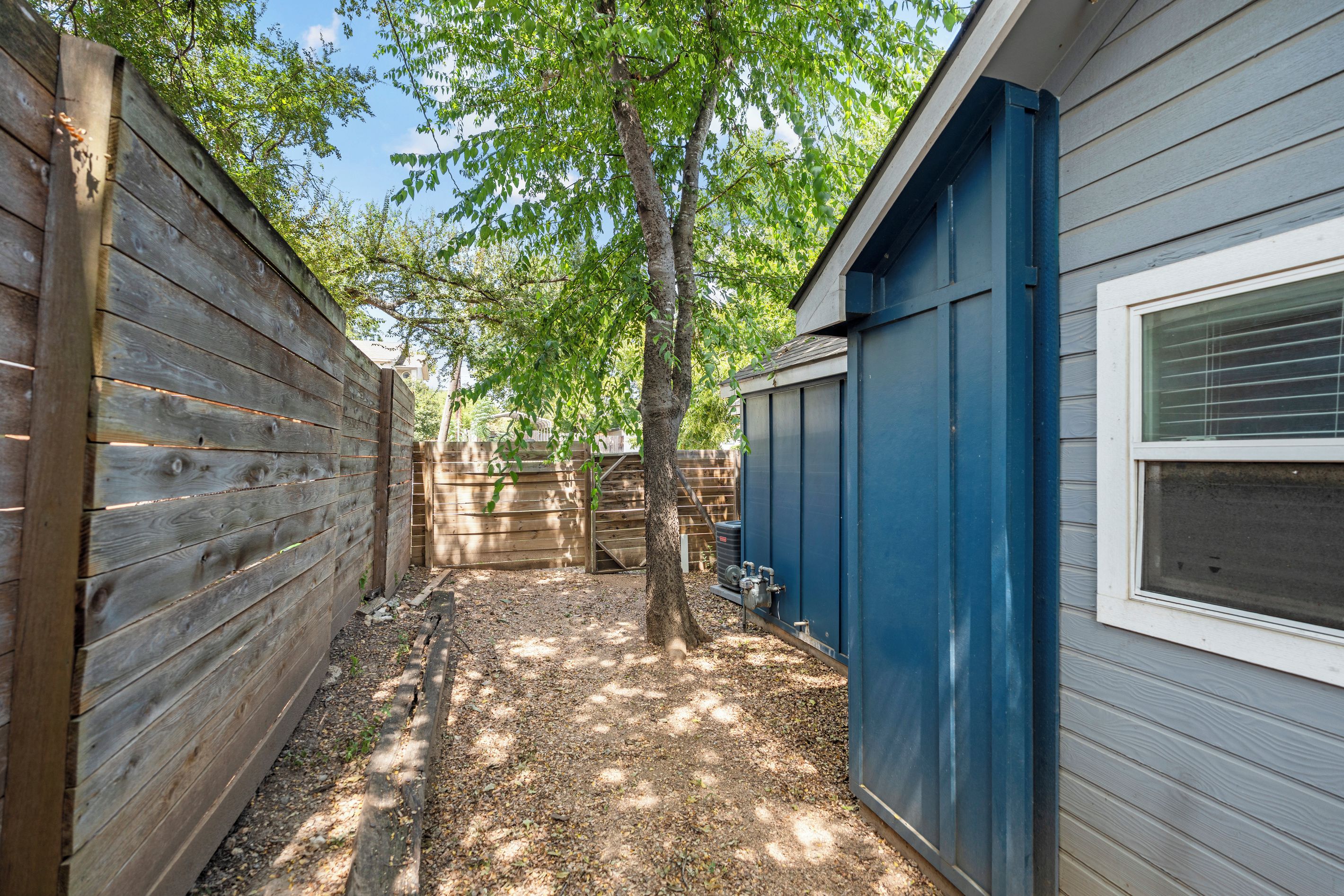 A narrow outdoor pathway flanked by wooden fences and a blue building with a window.