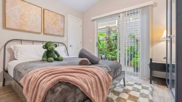 A bedroom with a bed, a teddy bear, a blanket, and a view of a balcony with plants.
