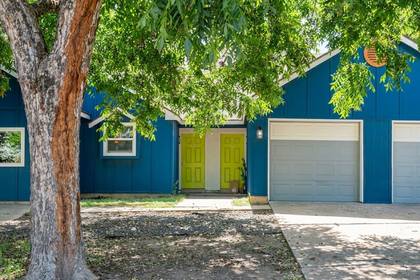A two-story house with a garage, a tree in the foreground, and a bright yellow door.