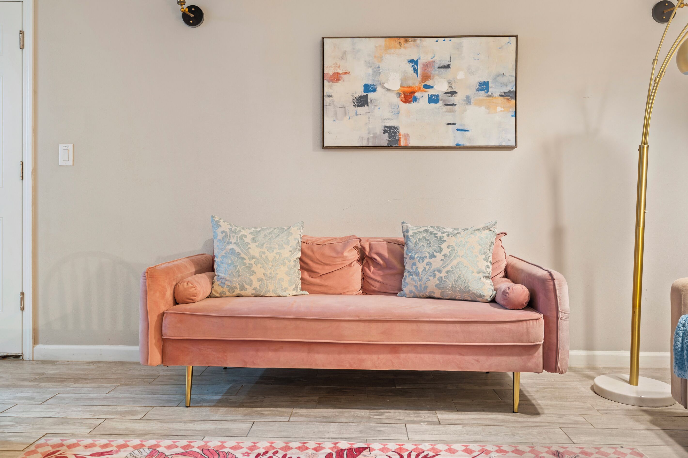 A pink sofa with patterned cushions, a modern floor lamp, and a contemporary abstract painting on the wall.