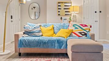 A living room with a sofa, a side table, a lamp, a mirror, and a door.