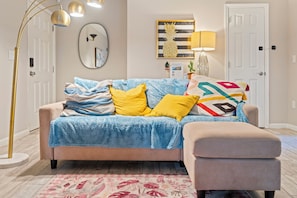 Ein Wohnzimmer mit einer Couch, einem Beistelltisch, einer Lampe, einem Spiegel und einer Tür.
