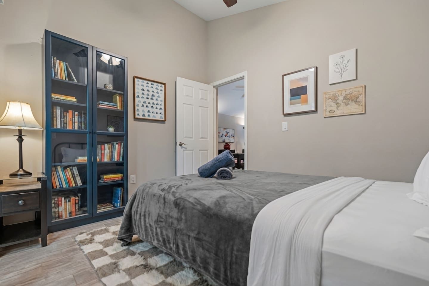 A bedroom with a bed, a bookshelf, a desk with a lamp, and a rug.