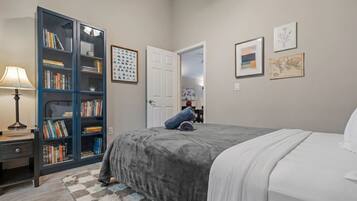 A bedroom with a bed, a bookshelf, a desk with a lamp, and a rug.