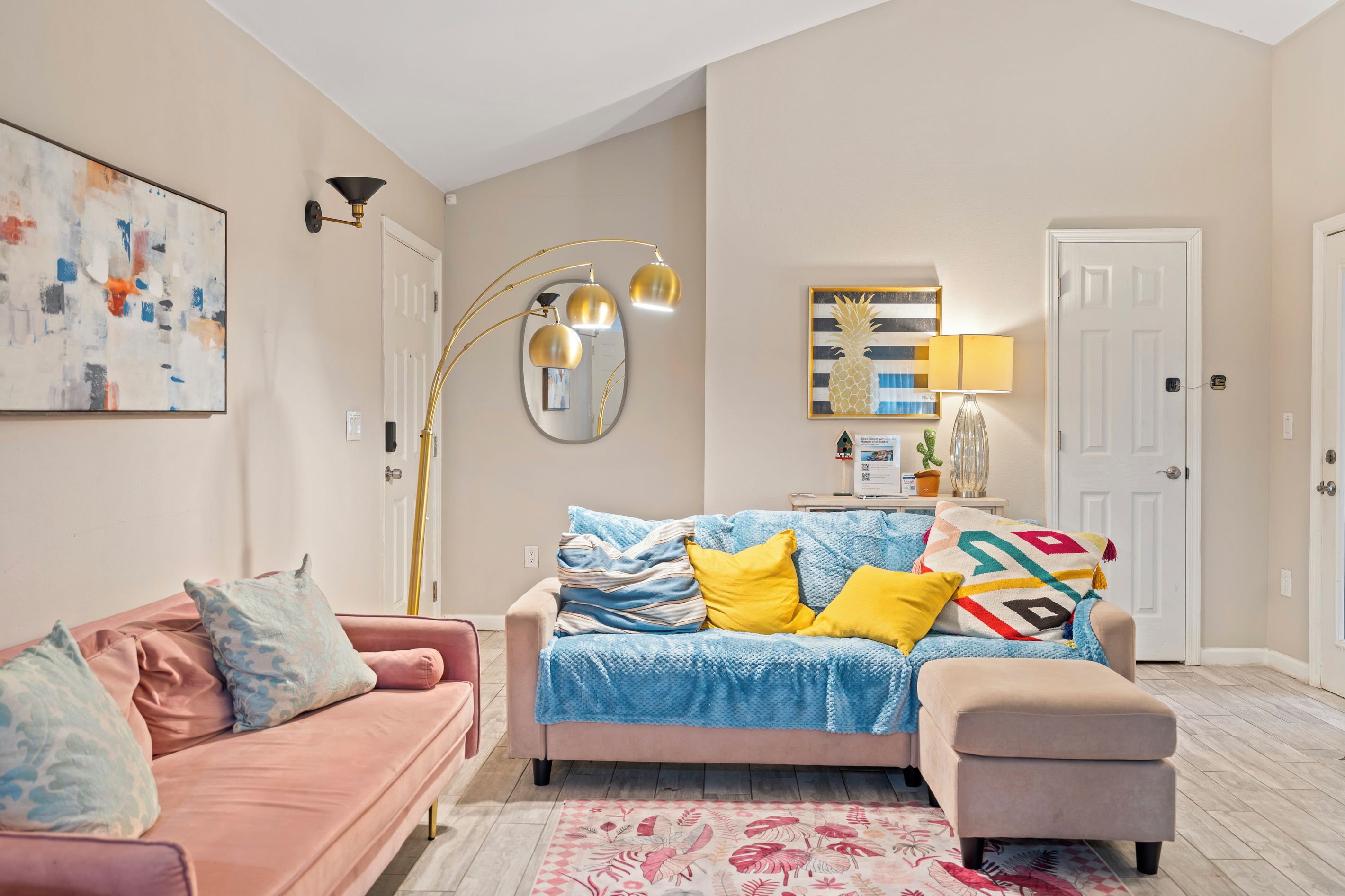 A living room with a pink sofa, a blue sofa, a coffee table, a floor lamp, a mirror, and a painting on the wall.