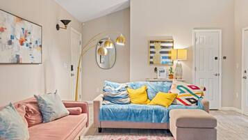 A living room with a pink sofa, a blue sofa, a coffee table, a floor lamp, a mirror, and a painting on the wall.