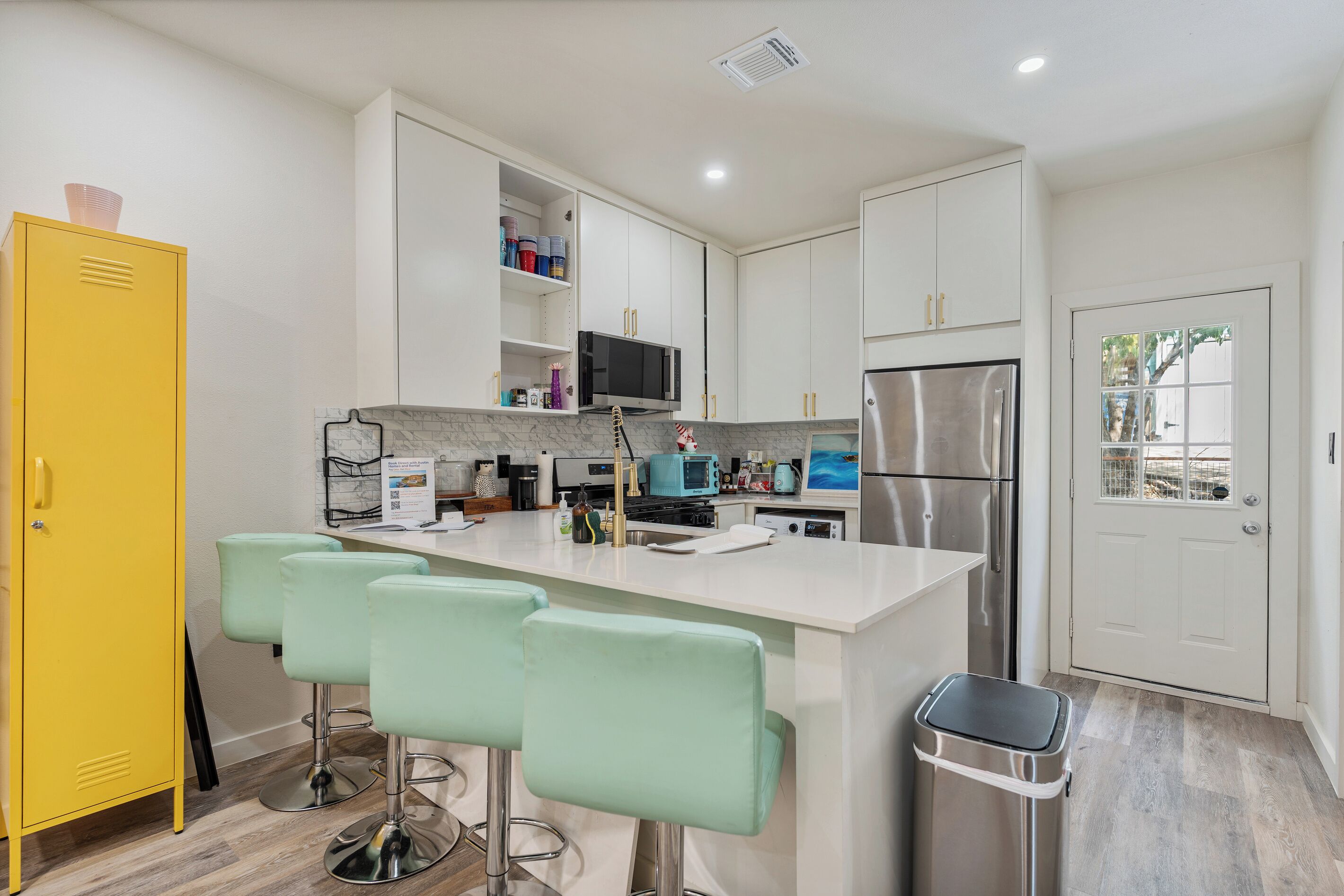 A modern kitchen with a central island, bar stools, a microwave, a refrigerator, and a trash bin.