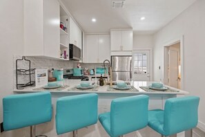 Een moderne keuken met witte kastjes, een roestvrijstalen koelkast en een centraal eiland met teal stoelen.