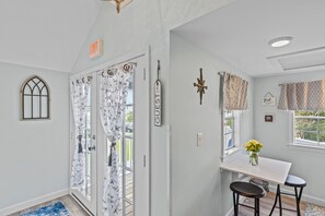 A bright room with a white door, a small table with a vase of flowers, and two barstools. - Sparrows Nest - Nestled in the Heart of Oriental (Oriental)