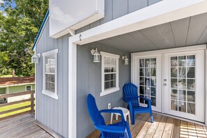 A covered porch with two blue Adirondack chairs and a small table, a white door with glass panels, and a wooden deck. - Sparrows Nest - Nestled in the Heart of Oriental (Oriental)