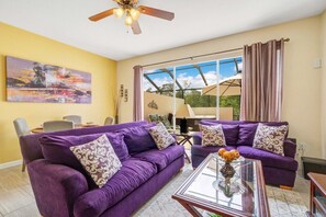 Ein Wohnzimmer mit violetten Sofas, einem Glastisch und einem Deckenventilator.