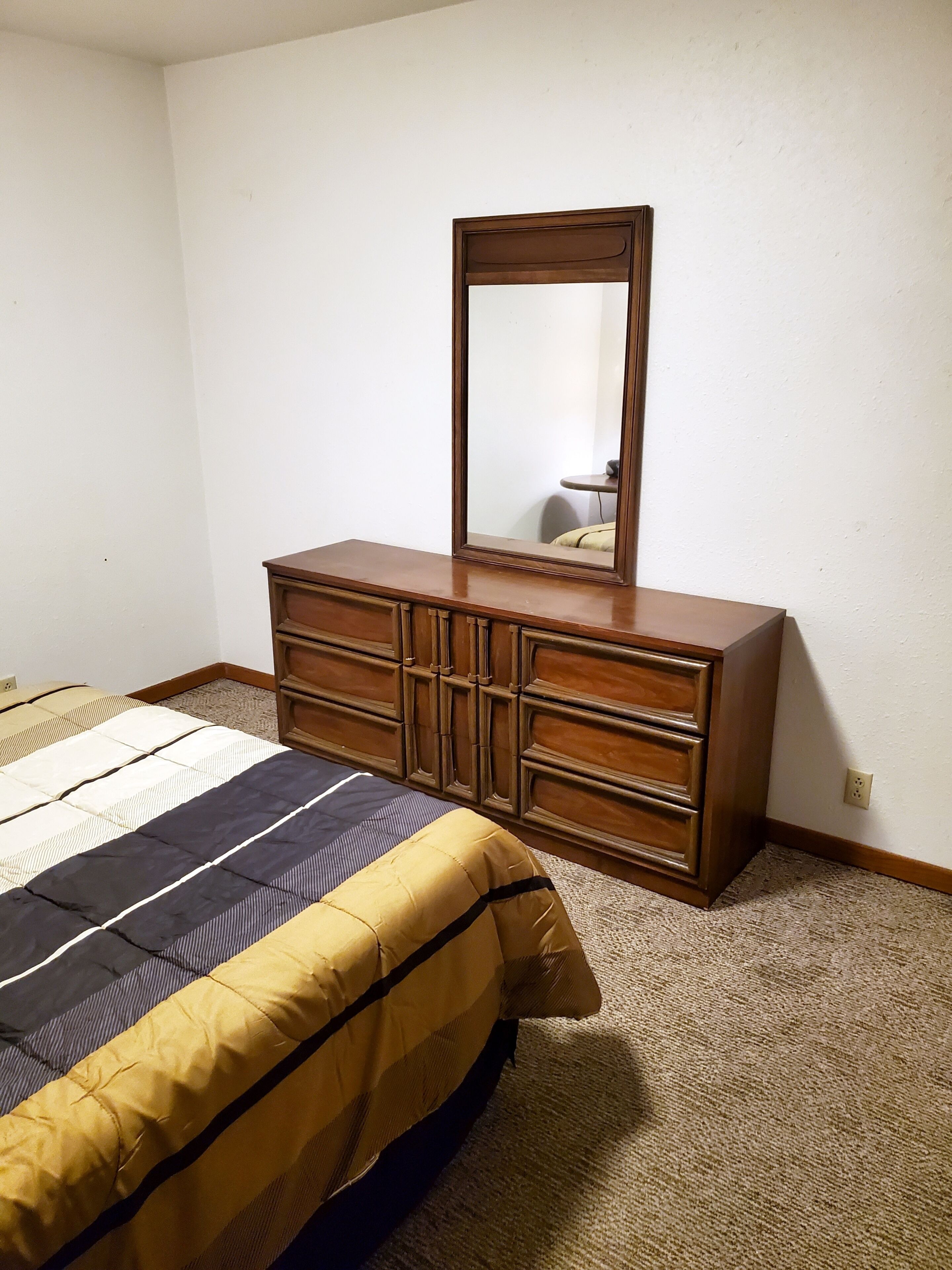 A bedroom with a bed, a wooden dresser, and a mirror.