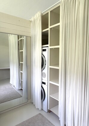 A laundry room with a washing machine, a mirror, and a storage cabinet.
