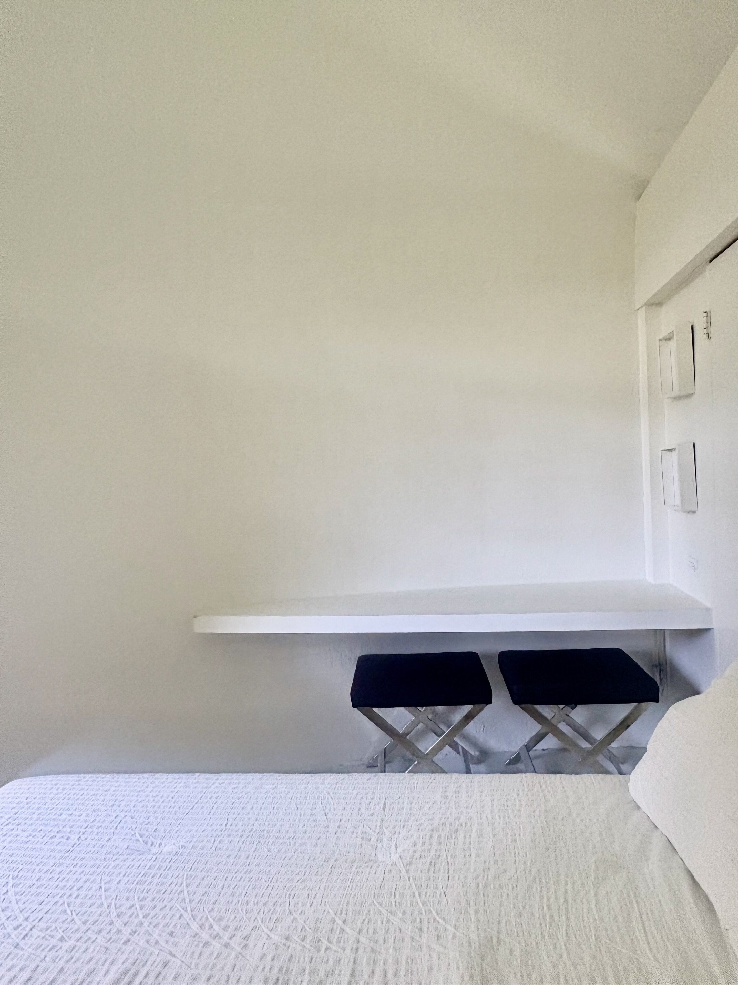 A room with a bed, a white desk, and two black chairs.