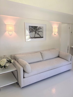 A modern living room with a light-colored sofa, a side table with a vase of flowers, and two wall-mounted light fixtures.
