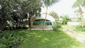 A building with a white exterior and a green awning, surrounded by lush greenery and palm trees.