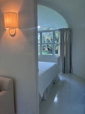 A bedroom with a bed, a window with curtains, and a wall-mounted light fixture.
