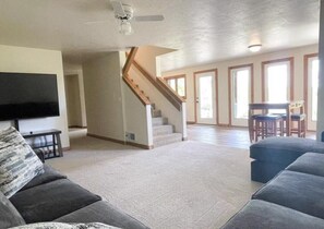 Ein geräumiges Wohnzimmer mit Treppe, einem Flachbildfernseher und einem Essbereich mit Stühlen.